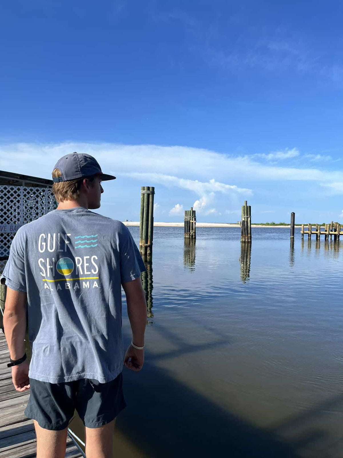 Person wearing a 'Gulf Shores, Alabama' t-shirt standing on a dock looking at the water.